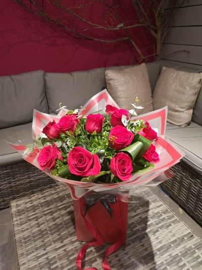 A dozen large red rose flower and foliage handtied bouquet in a gift bag