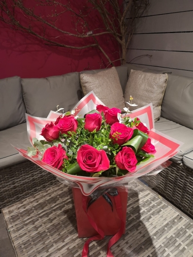 A dozen large red rose flower and foliage handtied bouquet in a gift bag